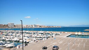 A marina with numerous boats docked, a parking area, and a clear view of the sea and distant mountains. - Selene: Renovated apartment in the port (L'Escala)