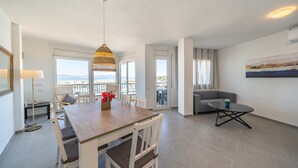 A modern living room with a wooden dining table, white chairs, a grey sofa, and a large window offering a view of the sea. - Selene: Renovated apartment in the port (L'Escala)