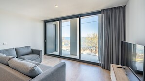 Een moderne woonkamer met een grijze bank, een houten salontafel en een grote schuifglazen deur die leidt naar een balkon.