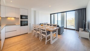 Een moderne keuken met witte kastjes, een eettafel met stoelen en een groot raam met uitzicht op de omgeving.