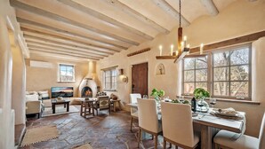 A rustic interior with a stone floor, wooden furniture, a fireplace, and large windows. - Luxurious Renovated Pueblo Style Home (Santa Fe)
