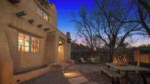 A rustic building with a stone patio, outdoor seating, and a large tree. - Luxurious Renovated Pueblo Style Home (Santa Fe)