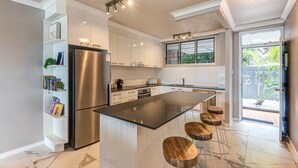 A modern kitchen with a central island, stainless steel appliances, and a view to the outdoors. - Frangipani Lodge F7, Frangipani Lodge F7 (Hamilton Island)