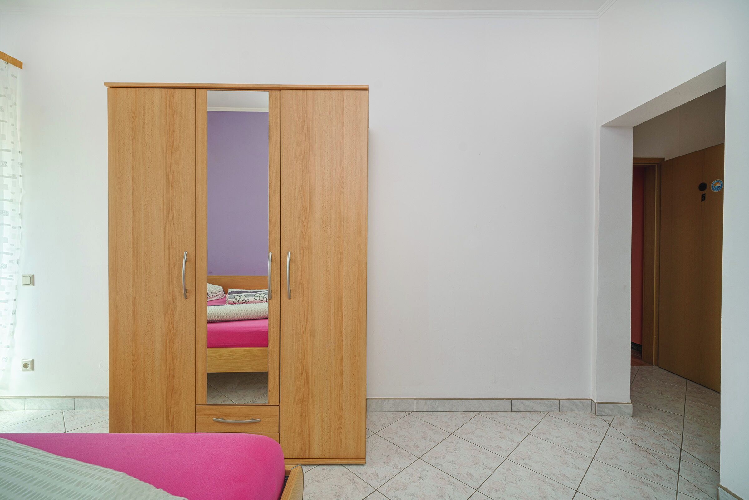 A bedroom with a wooden wardrobe, a bed with a pink bedspread, and a purple wall.