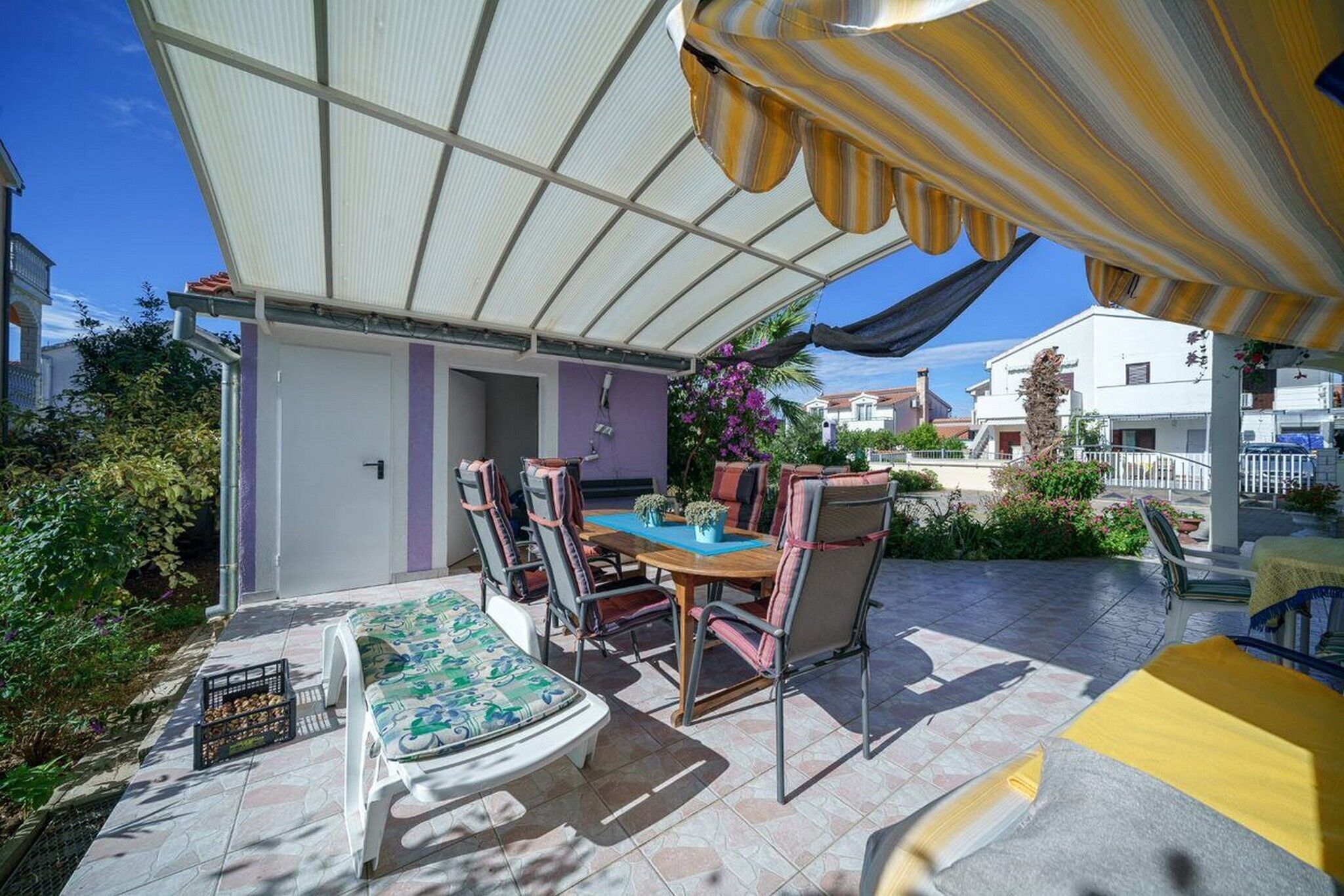A covered patio with a table and chairs, a sofa, and a small garden area.