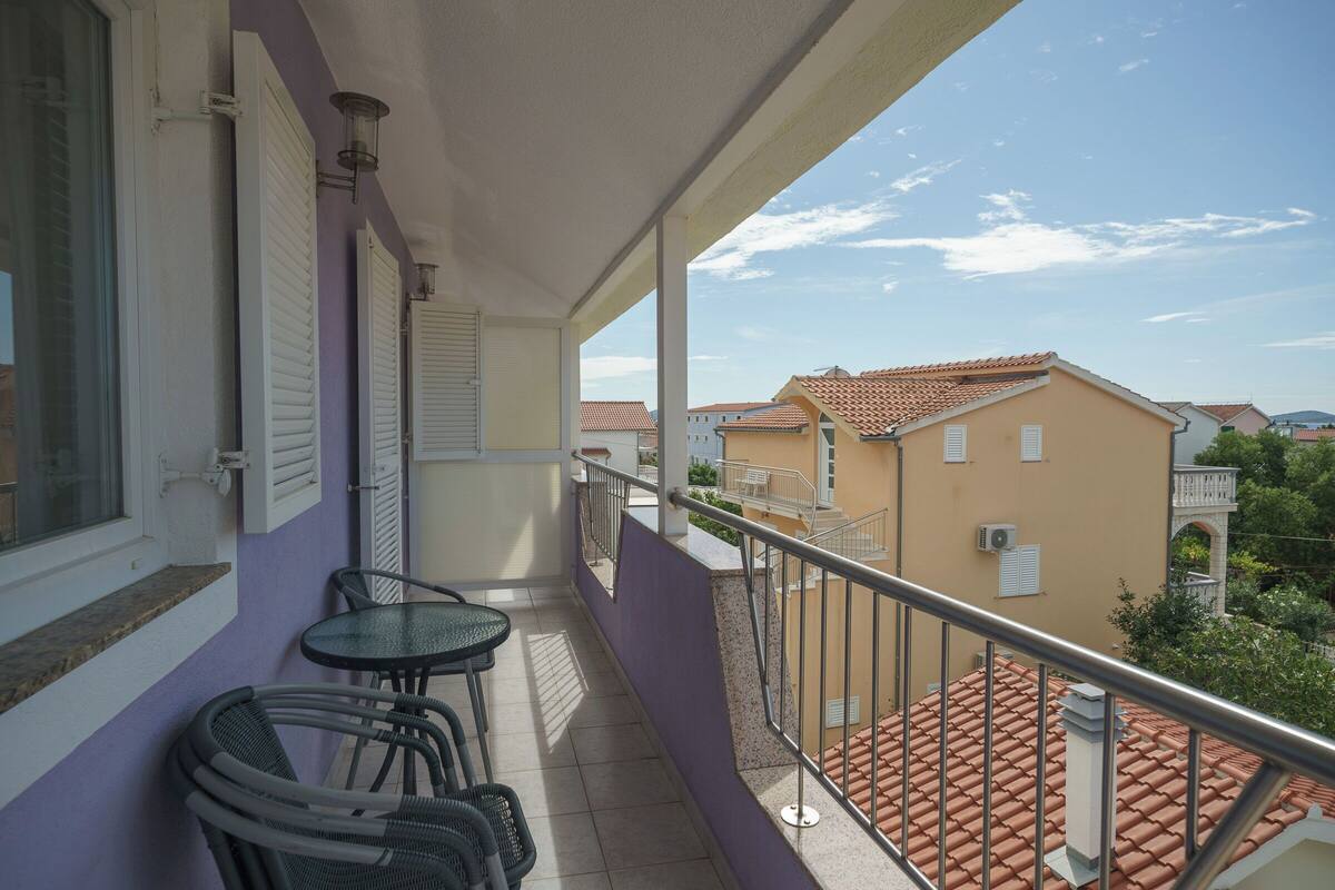 Un balcon avec une table et des chaises, une vue sur les immeubles voisins et un ciel dégagé.