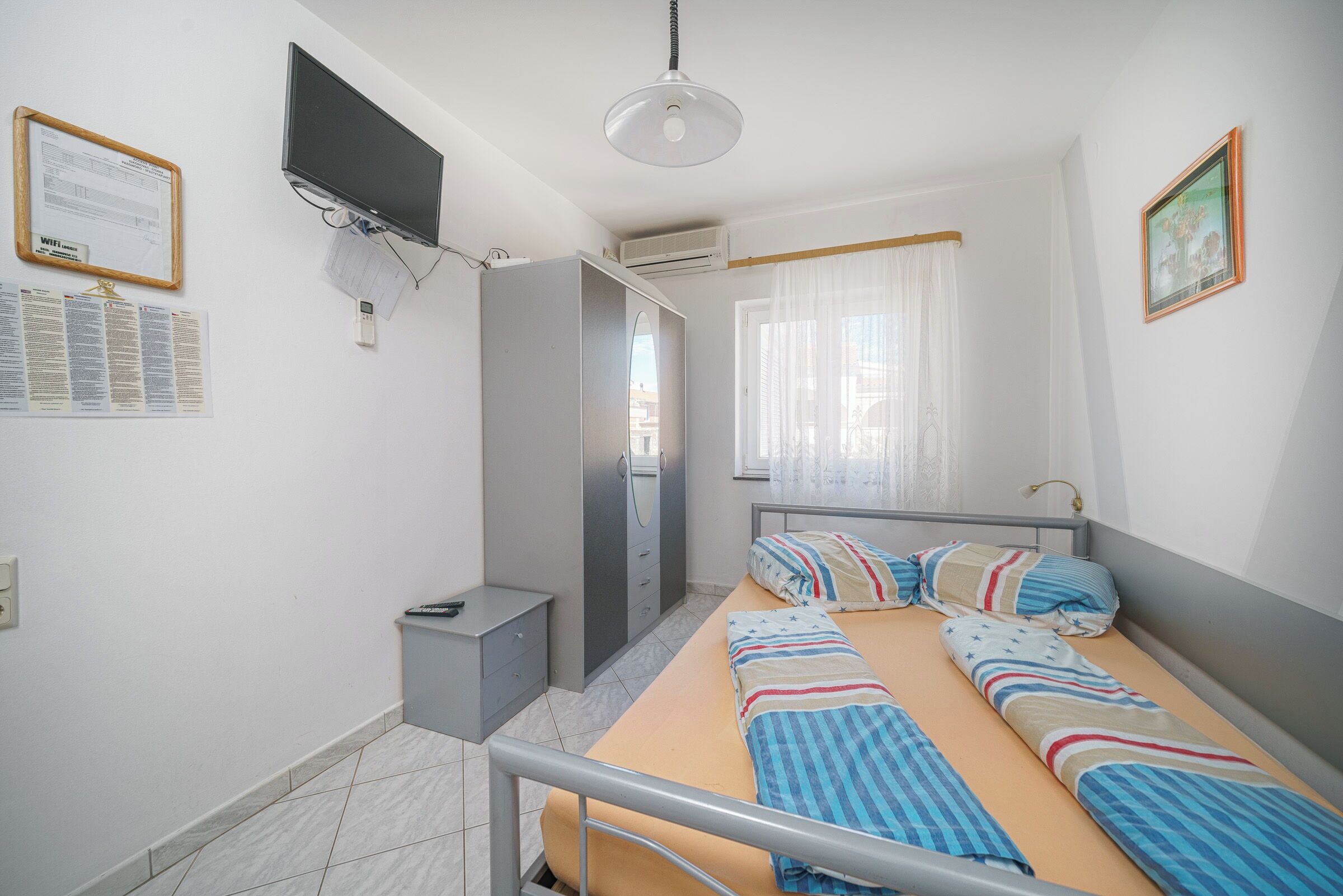 A bedroom with a bed, a wardrobe, a desk, a TV, and a window with curtains.