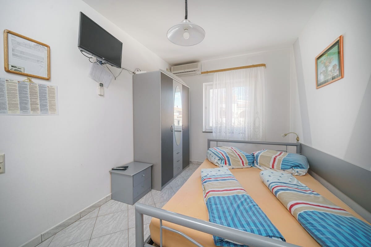 Une chambre à coucher comprenant un lit, une armoire, un bureau, un téléviseur et une fenêtre avec des rideaux.