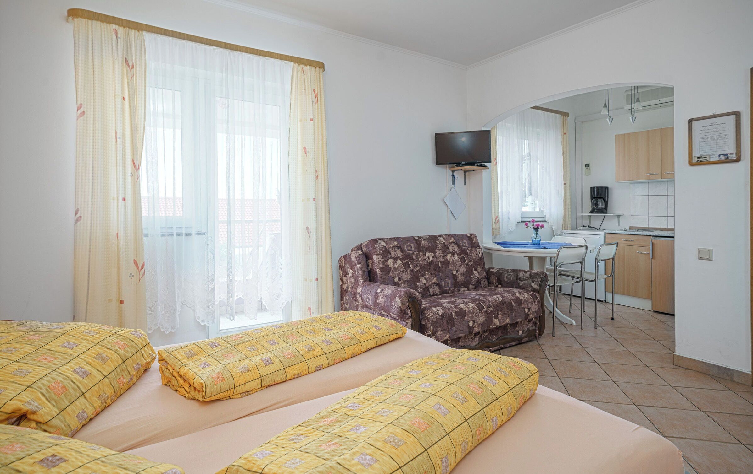 A hotel room with two beds, a sofa, a TV, a small kitchen, and a dining area.