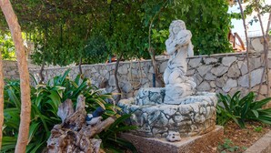 A stone statue of a woman on a pedestal surrounded by greenery and a rustic tree trunk. - Apartment Jakov (Rogac)