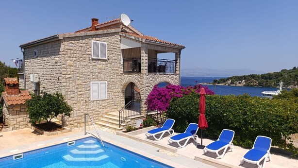A stone building with a pool and lounge chairs, overlooking a body of water. - Apartment Jakov (Rogac)