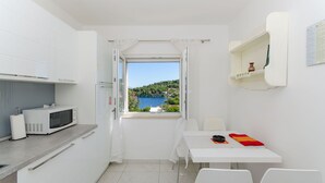 A small, bright kitchen with a view of a lake and hills, white cabinets, a microwave, and a table with chairs. - Apartment Jakov (Rogac)