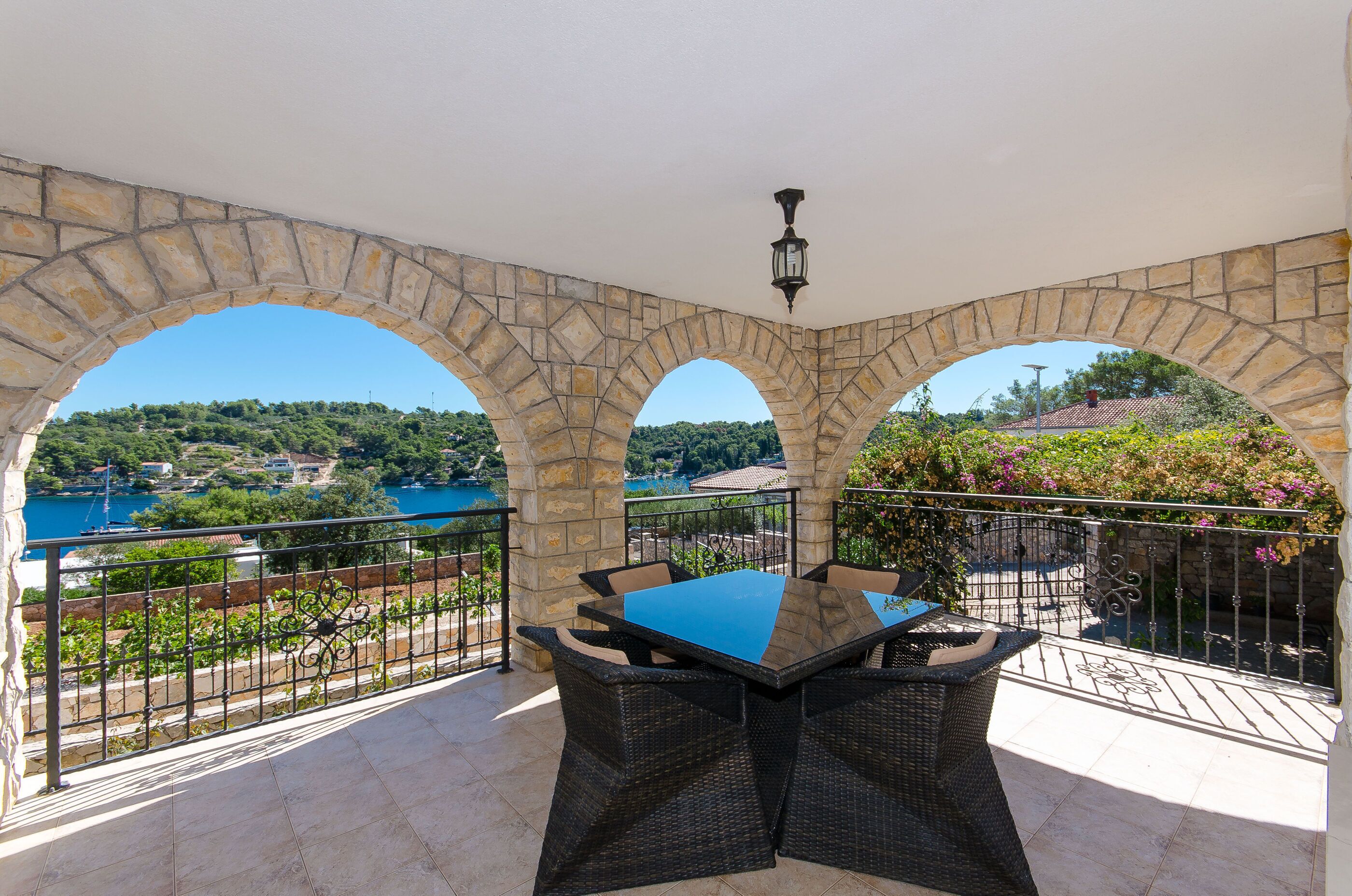 Una terrazza con archi in pietra, un tavolo e sedie, con vista su un lago e sulla vegetazione.