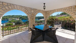 A terrace with stone arches, a table, and chairs, overlooking a lake and greenery. - Apartment Jakov (Rogac)