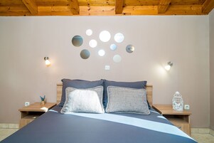 Quarto com cama, duas mesinhas de cabeceira, luminária fixa na parede e teto com vigas de madeira.