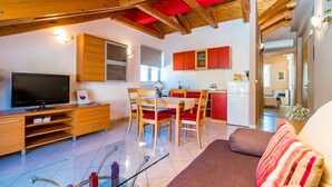 A modern living room with a TV, wooden furniture, and a kitchen in the background. - Apartments Kruno (Zaton)