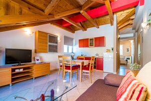 Uma sala de estar moderna com televisão, móveis de madeira e uma cozinha ao fundo.