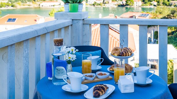 A breakfast table with croissants, orange juice, and coffee cups on a balcony overlooking a lake. - Apartments Kruno (Zaton)