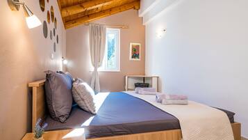 Un dormitorio con techo de madera, una cama con colchón azul oscuro, una manta color crema y una mesita de noche con una lámpara.