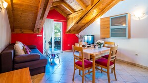 A cozy room with a wooden ceiling, a red wall, a sofa, a dining table with chairs, and a TV. - Apartments Kruno (Zaton)