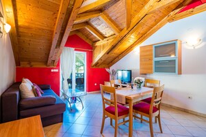 Um quarto aconchegante com teto de madeira, parede vermelha, sofá, mesa de jantar com cadeiras e uma TV.