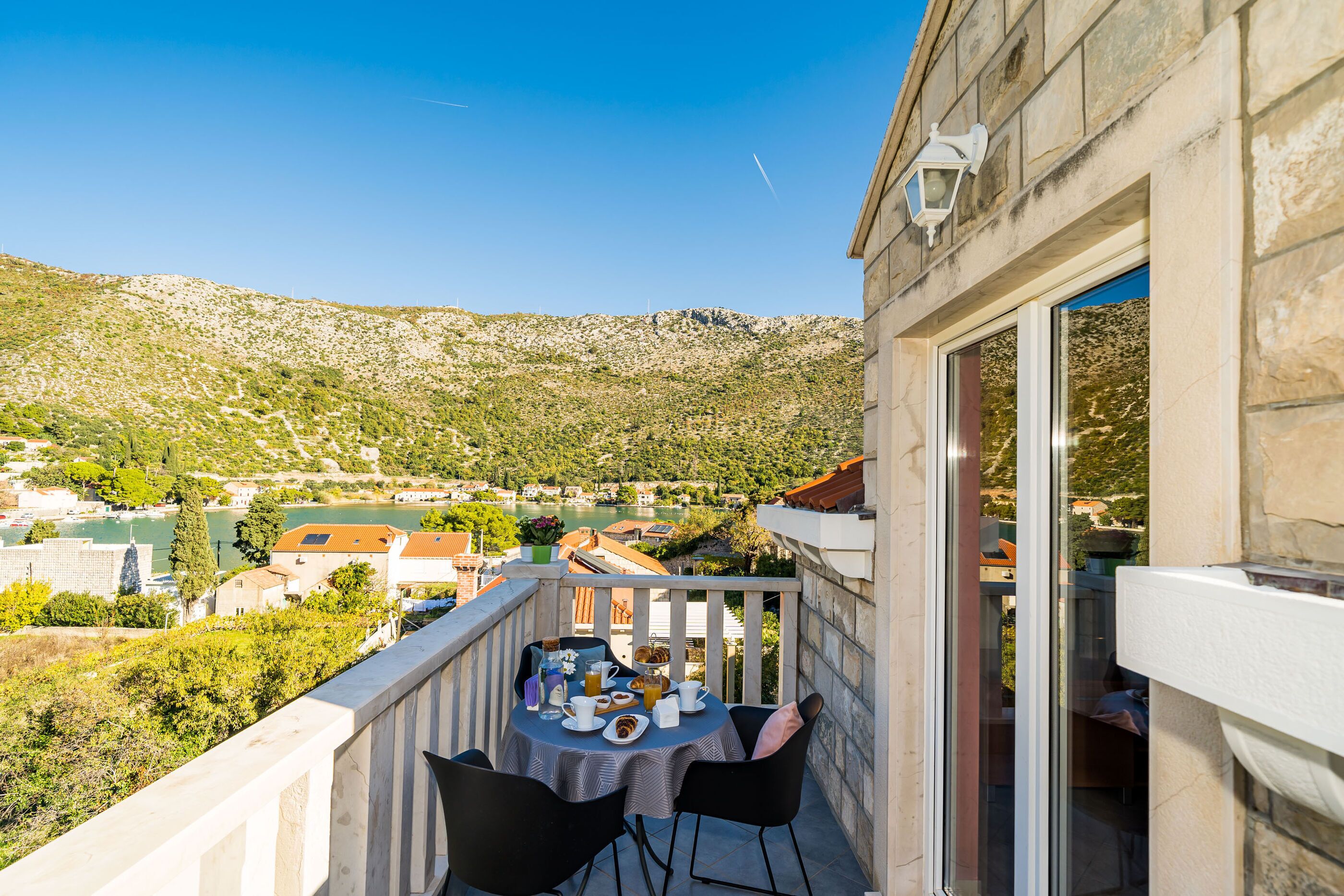 A balcony with a table set for two, overlooking a scenic hillside view.