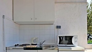Une cuisine compacte avec des meubles blancs, un évier, une bouilloire et un four à micro-ondes.