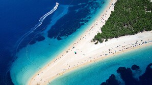 Vista aerea di una spiaggia con acque turchesi cristalline, una battigia sabbiosa e una fitta area boschiva alla destra.