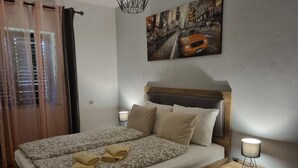 Un letto rifatto con cura, con lenzuola a fantasia e due cuscini, una lampada da comodino e un quadro raffigurante un panorama urbano sulla parete.
