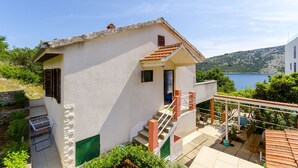 Ein zweistöckiges Haus mit Balkon und Blick auf einen See, einer Treppe mit roten Geländern und einem kleinen Garten.