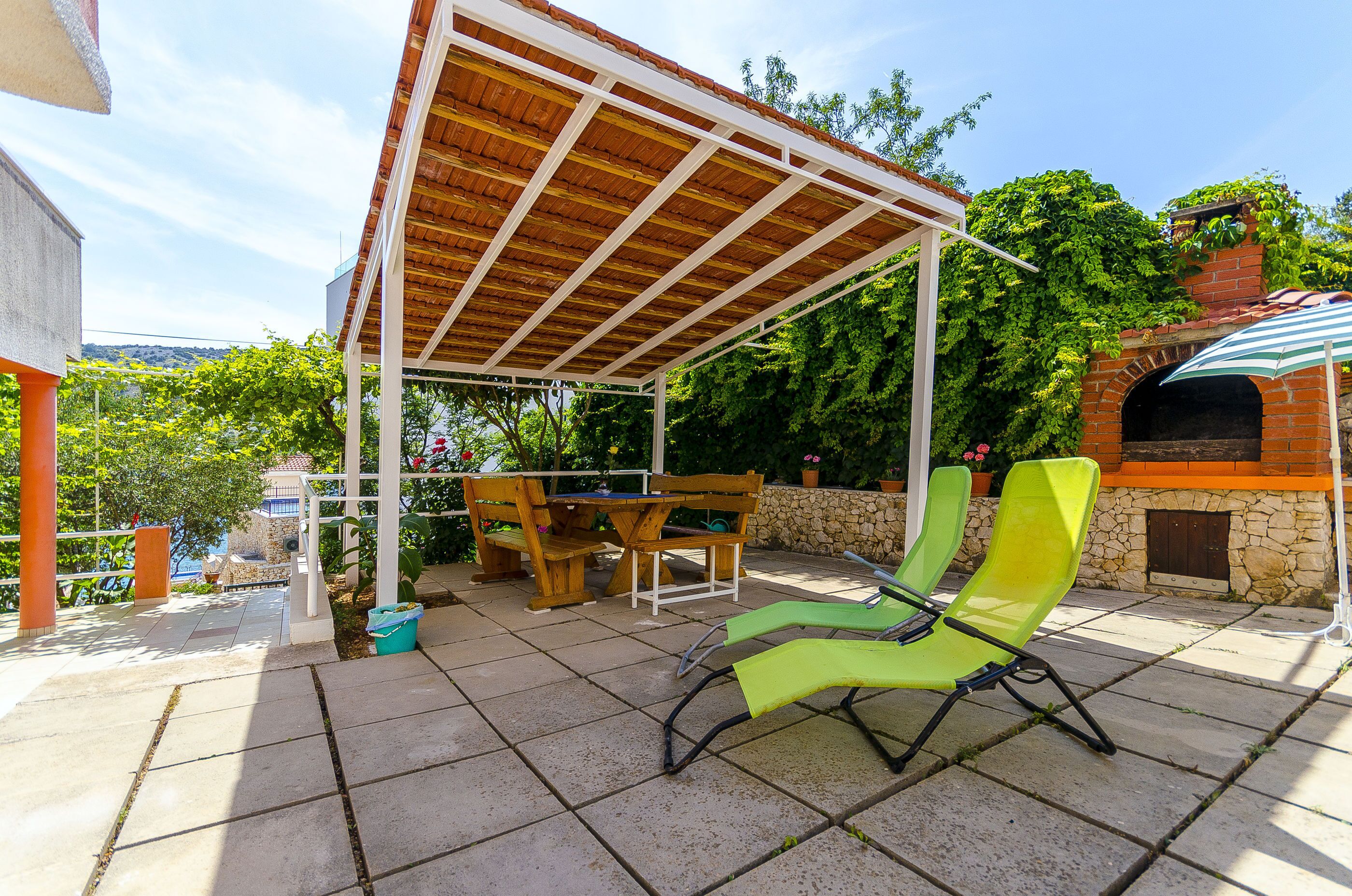 Eine Außenpatio mit einer Holz-Pergola, einer Steinmauer und einem Backofen aus Ziegeln.