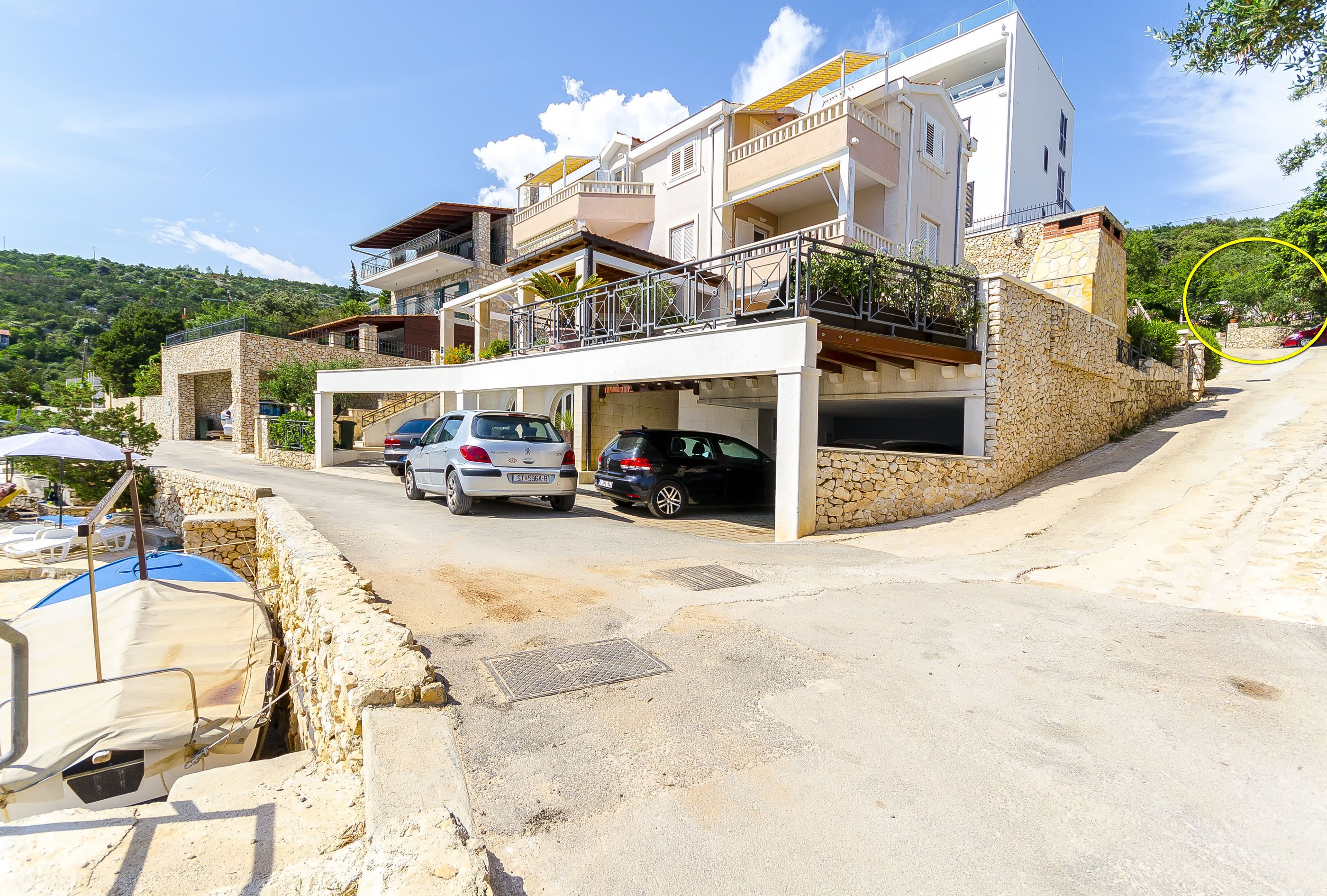 A multi-story building with a parking area, stone walls, and a view of a hilly landscape.