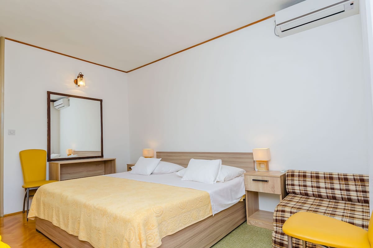 Une chambre à coucher comprenant un lit, des lampes de chevet, un miroir, une chaise et un appareil de climatisation.