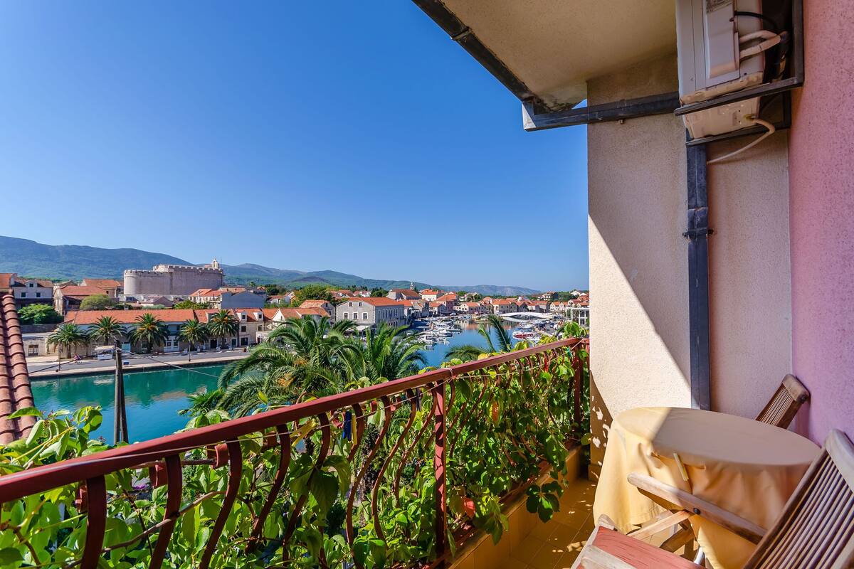 Un balcon offrant une vue sur un port de plaisance, des immeubles et un château situé au loin.