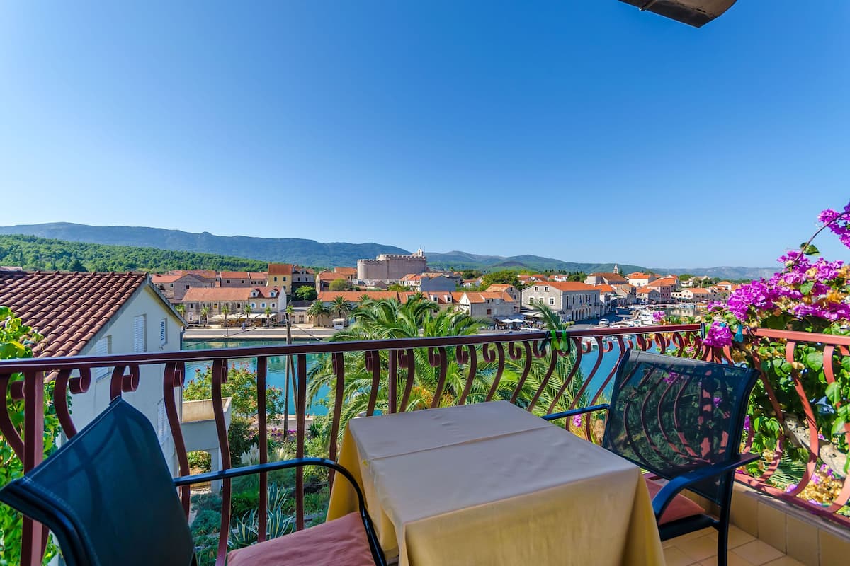 Un balcon avec une table et des chaises, d’où l’on peut admirer une ville avec ses bâtiments et, au loin, des montagnes.