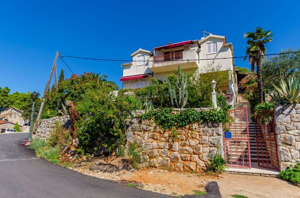A two-story house with a stone wall, a red gate, and a clear blue sky. - Apartments and Rooms Darinka (Vrboska)