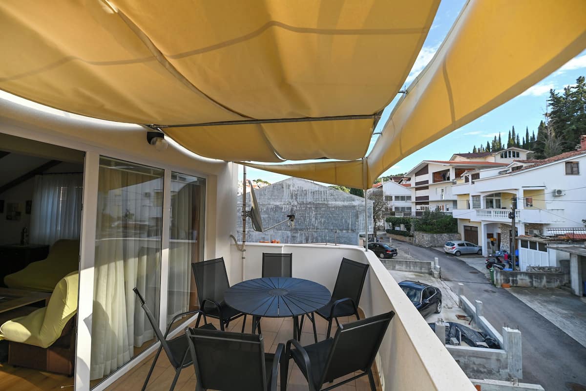 A balcony with a table and chairs, a yellow canopy, and a view of the street and buildings.