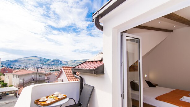 Un balcon avec une table préparée pour le petit-déjeuner, un lit et une vue sur la ville et les montagnes.