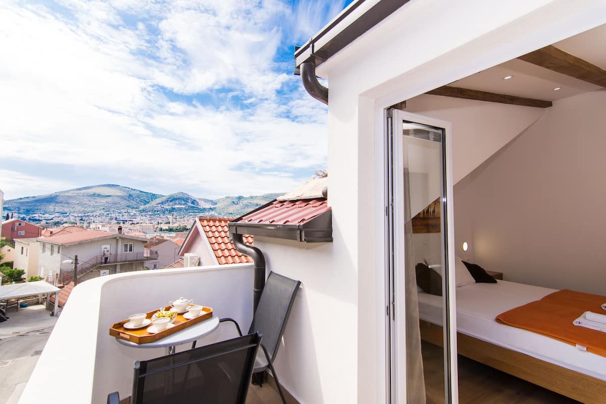 A balcony with a table set for breakfast, a bed, and a view of the city and mountains.
