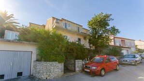 A residential street with a red car parked in front of a house, a stone wall, and a gate. - Apartment Town View (Korcula)