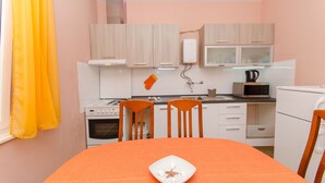 A compact kitchen with white cabinets, a microwave, and a stove. There is a table with a single plate and a chair. - Apartment Town View (Korcula)