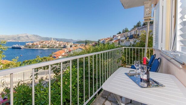 A balcony with a table set for two, overlooking a coastal town and the sea. - Apartment Town View (Korcula)