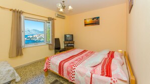 A bedroom with a bed, a TV, a window with a view of a coastal town, and a ceiling fan. - Apartment Town View (Korcula)