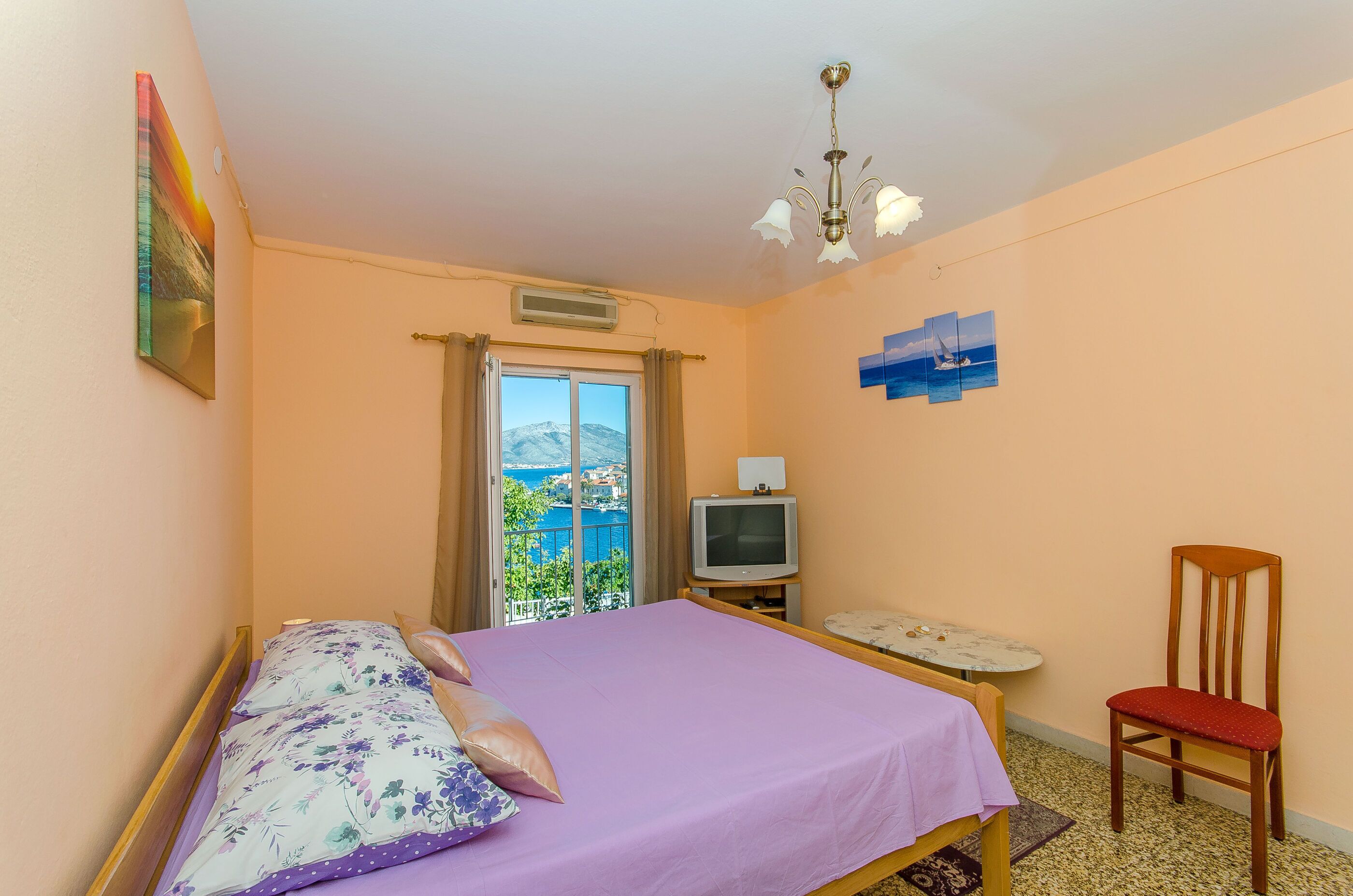 A bedroom with a bed, a TV, a chair, and a view of the sea.