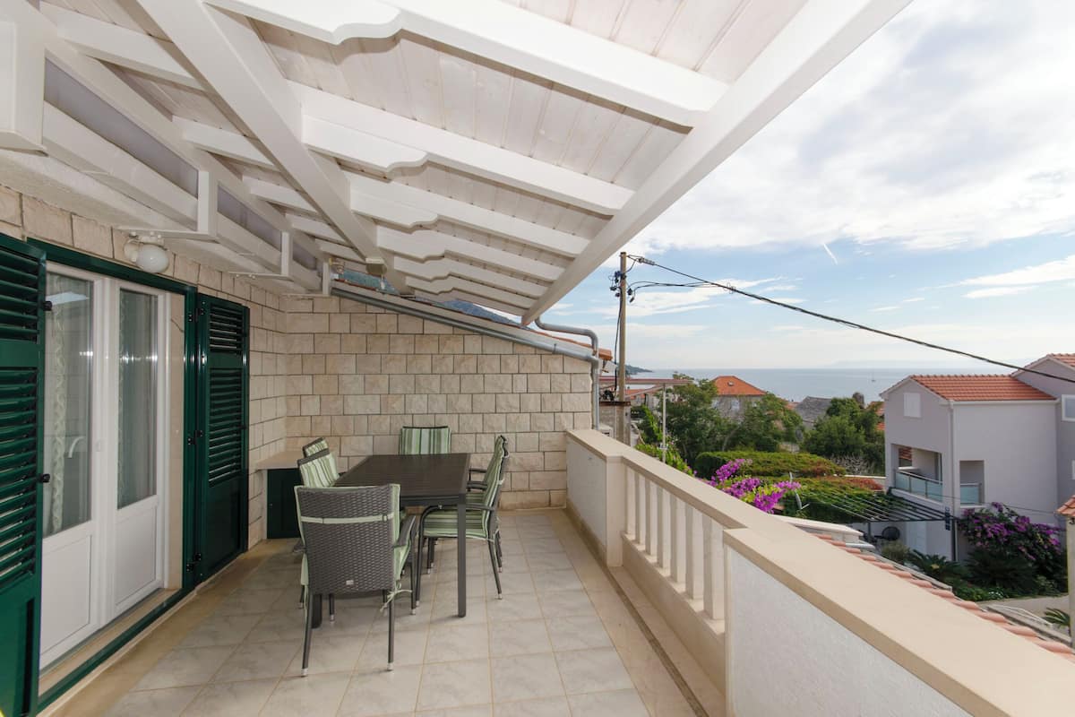 A balcony with a table and chairs, a view of the sea, and a stone wall.