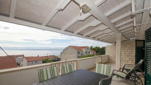Un patio techado al aire libre con una mesa y sillas, con vistas a una zona residencial con casas y al mar.
