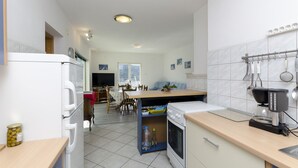 A modern kitchen with a built-in oven, a coffee maker, and a dining area with a table and chairs. - Apartments Bilo (Marina)
