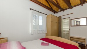 A bedroom with a bed, a wardrobe, a window with curtains, and a mirror on the wall. - Apartments Bilo (Marina)