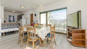 A dining area with a round table, wooden chairs, and a TV on a wooden stand. - Apartments Bilo (Marina)