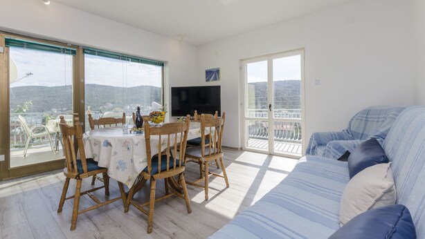 A bright living room with a balcony, a dining table with chairs, a sofa, and a TV. - Apartments Bilo (Marina)